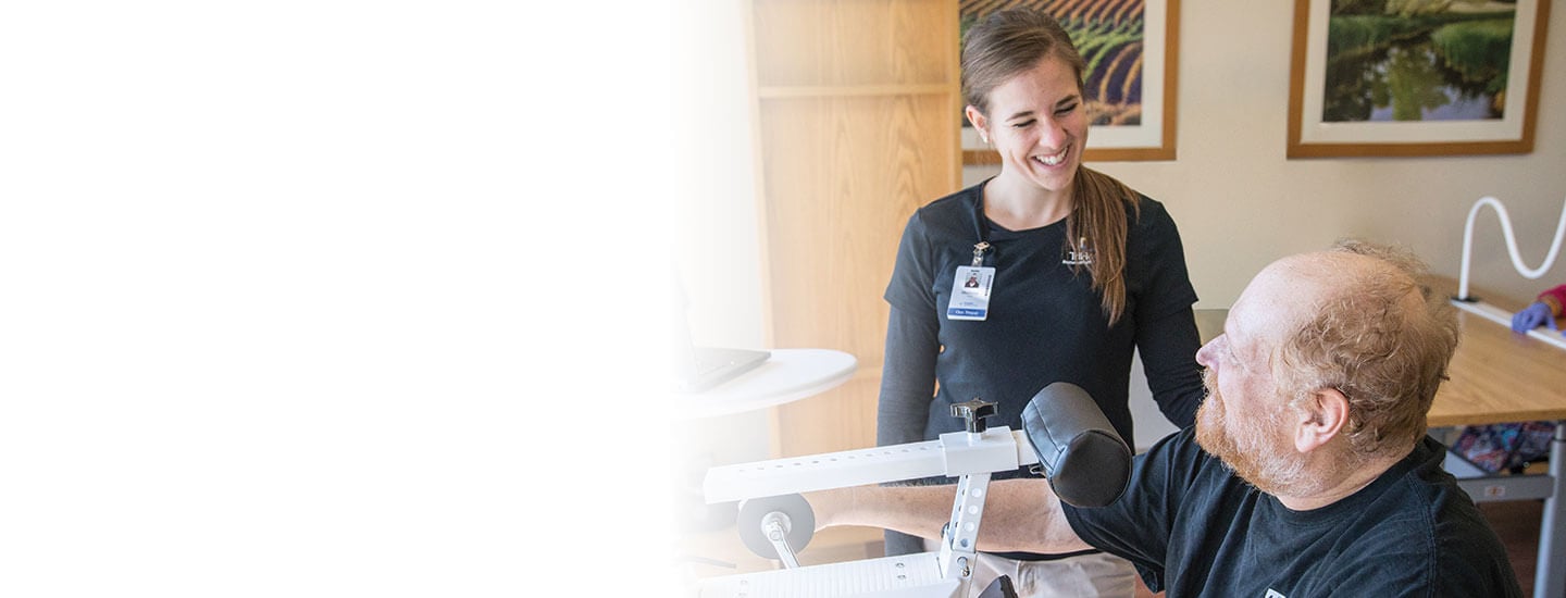 A female nurse smiles at her male patient as he has a therapy session working on arm strength.